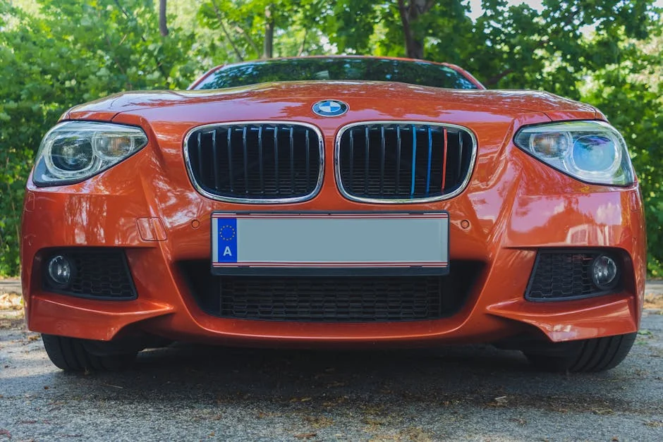 Low angle shot of an orange BMW car front, parked outdoors with green foliage background. - affordable luxury daily goods that feel highend