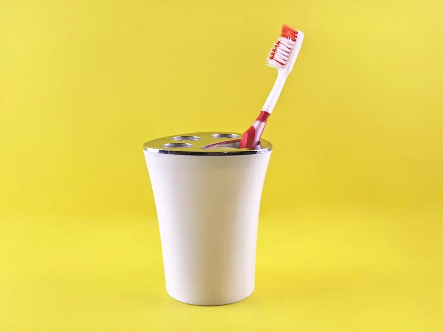 Simple white toothbrush holder with red toothbrush on vibrant yellow background. - best budgetfriendly daily essentials for homeowners 2026