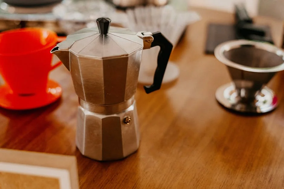 High-angle view of a classic Italian moka pot surrounded by coffee accessories on a wooden table. - how to choose the right coffee maker for your morning routine
