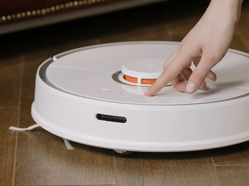 Close-up of a hand pressing a button on a robotic vacuum cleaner on a wooden floor. - comprehensive review of the latest smart home cleaning devices