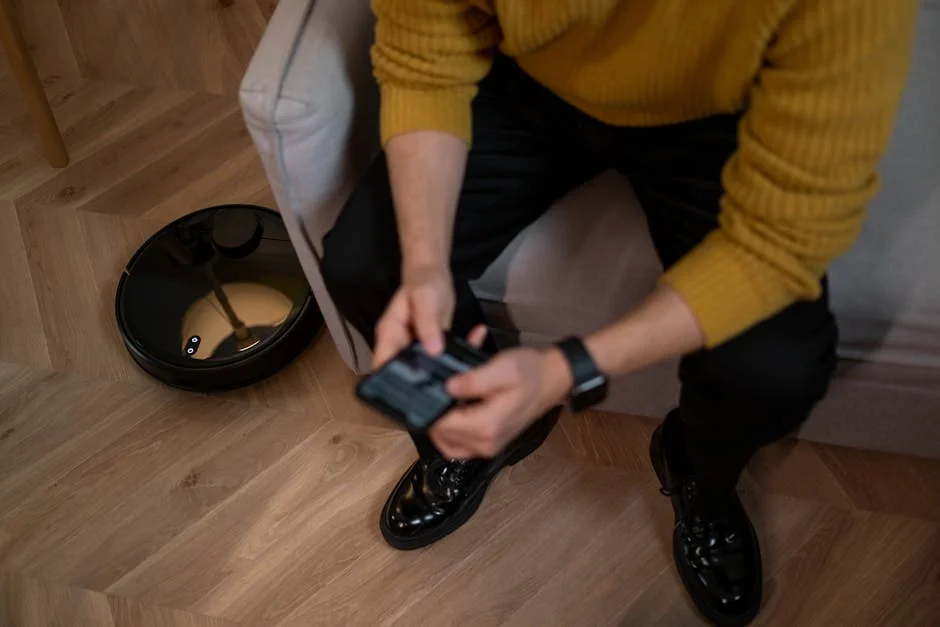 Man in yellow sweater using remote to control robotic vacuum on wooden floor. - comprehensive review of the latest smart home cleaning devices