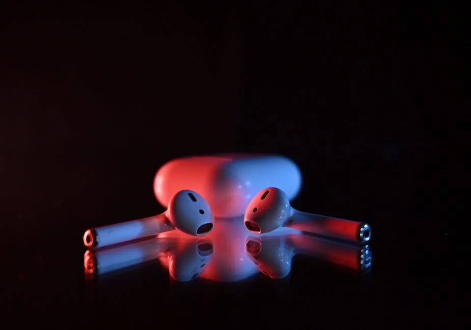 Wireless earbuds in a dramatic red and blue lighting on a reflective surface. - factors to consider before upgrading your daily tech gadgets
