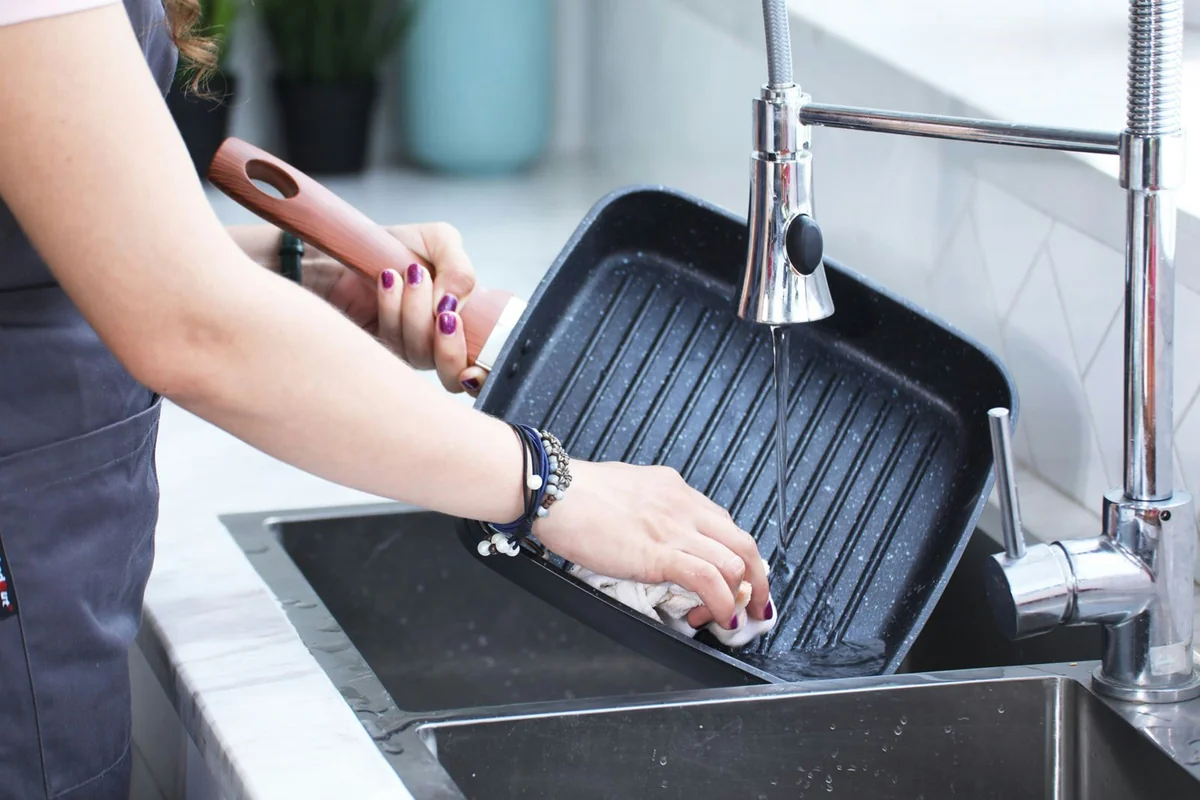 a woman washing a grill in a kitchen sink - how to spot highquality materials in everyday household goods