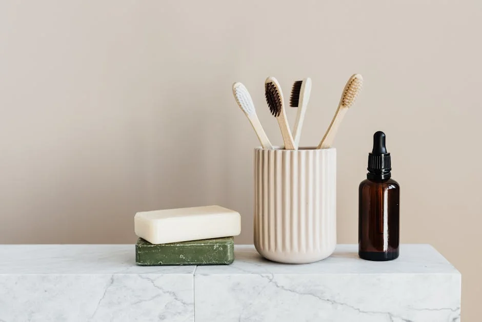 Collection of organic soaps and bamboo toothbrushes in ceramic minimalism style holder placed near renewable glass bottle with essential oil on white marble tabletop against beige wall - sustainable and plasticfree bathroom essentials review