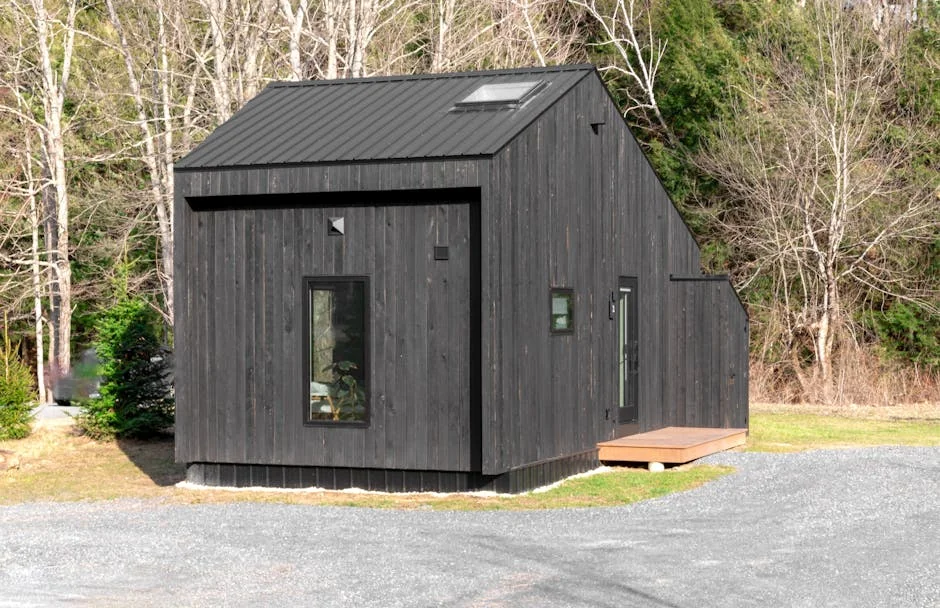 A minimalistic black tiny house nestled in a forest area, showcasing sustainable living. - top spacesaving gadgets for tiny house living